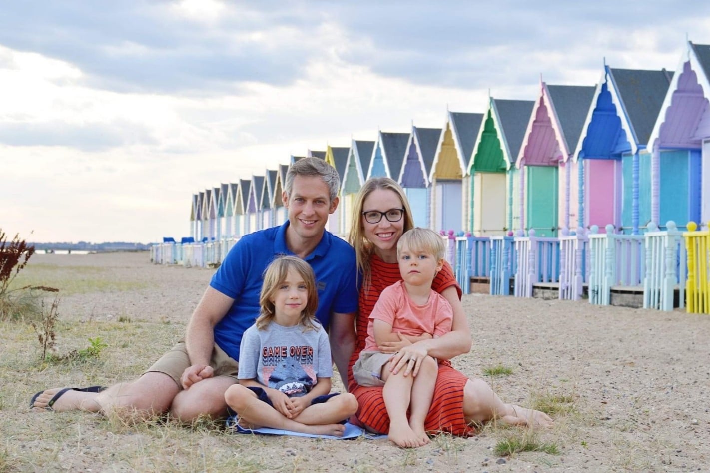 Mum, Dad and 2 children sitting on a beach in front of beach huts
